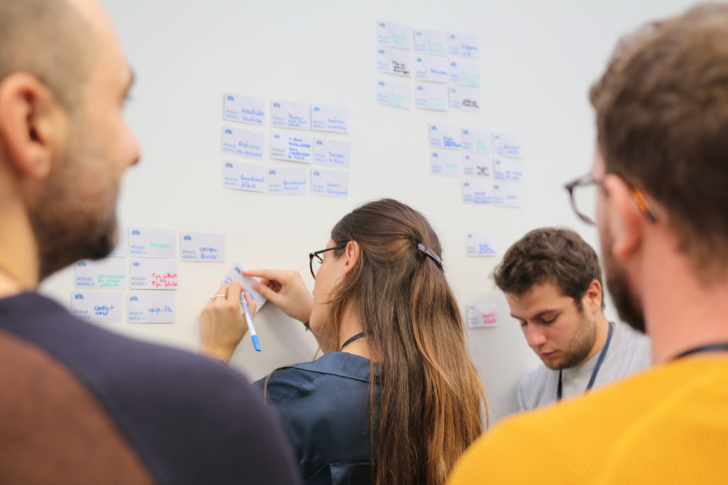 Femme de dos en train d'écrire sur un post-it collé au mur - UXcamp 2018